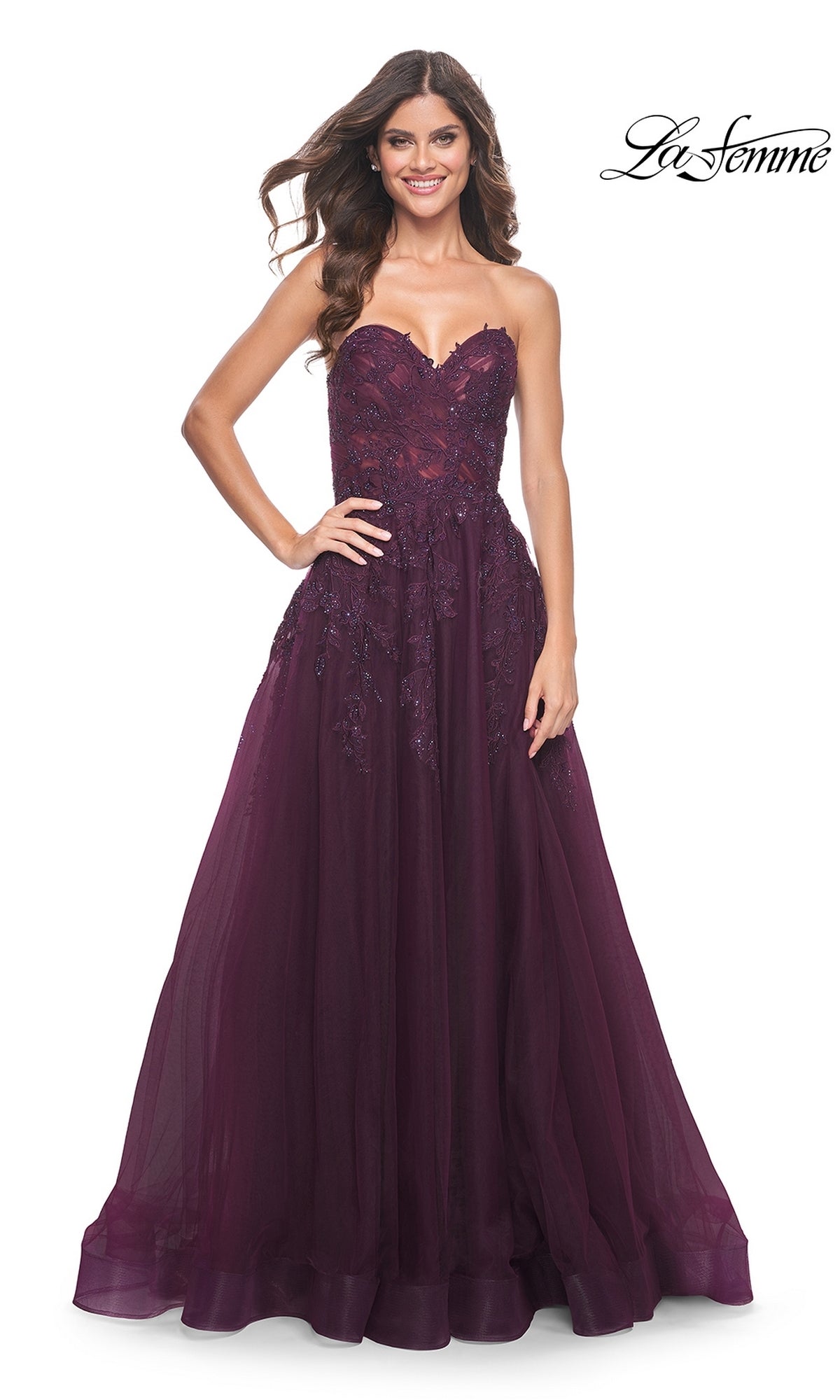 Woman wearing the La Femme Lace-Up Long Sweetheart Prom Dress 32304 in deep purple with lace and tulle details, smiling. This elegant strapless A-line gown adds grace. La Femme logo appears in the top right corner.